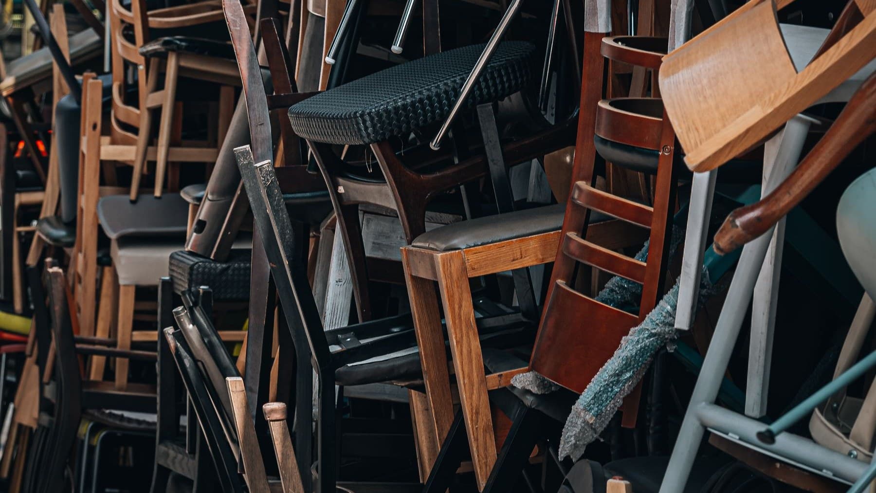 Dense stack of discarded wooden and plastic chairs piled together awaiting collection