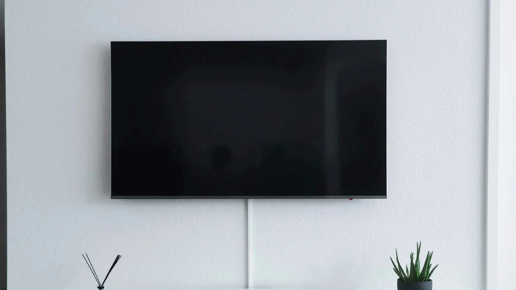 Wall-mounted flat screen television with a blank screen and a single cable running down a plain white living room wall