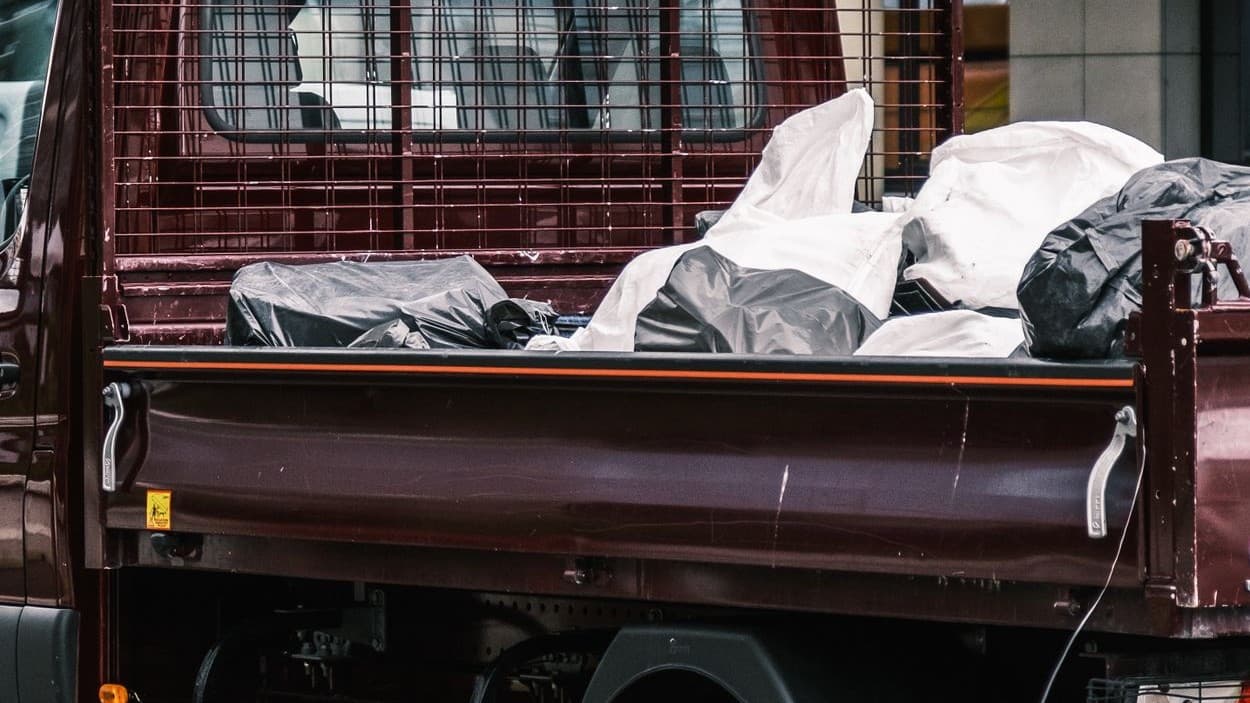 Open flatbed truck bed part-loaded with black and white bagged waste behind a mesh headboard