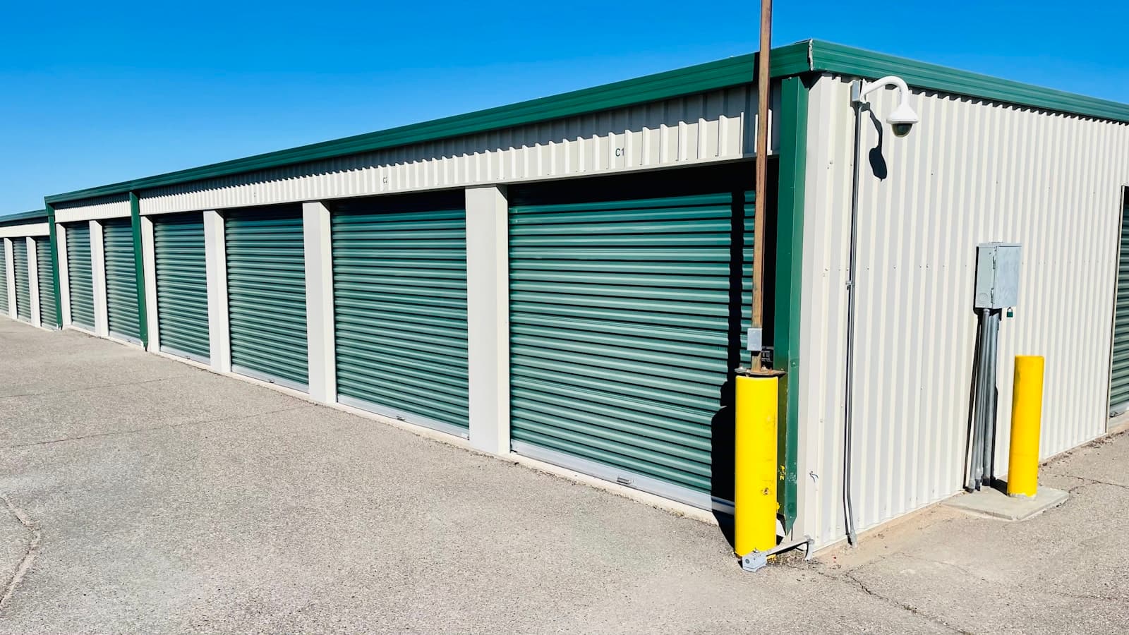 Row of green roller-shutter doors along a single-storey self-storage building under a clear sky