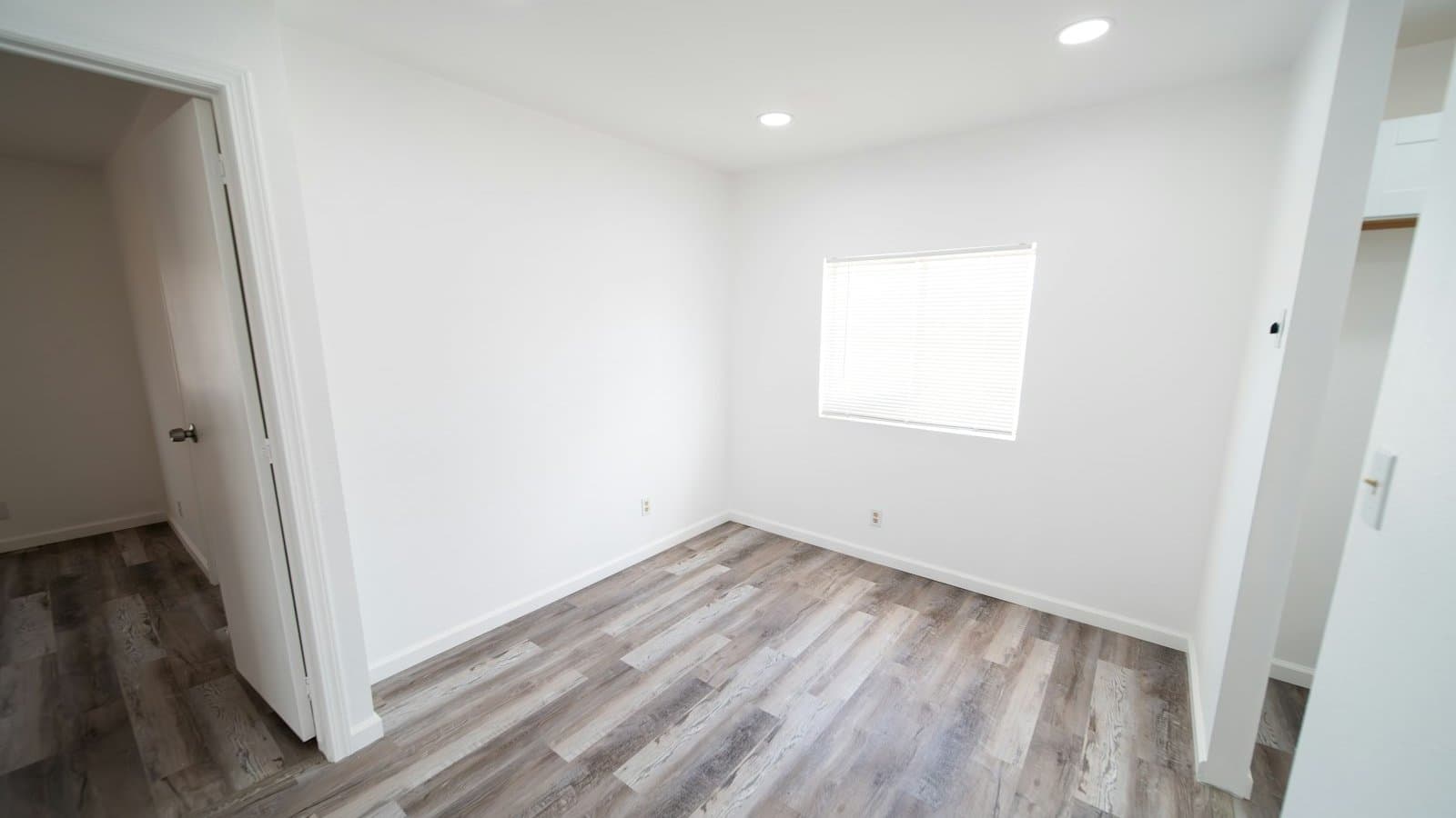 Empty villa bedroom with light wood-look flooring, white walls and a window, cleared of all furniture