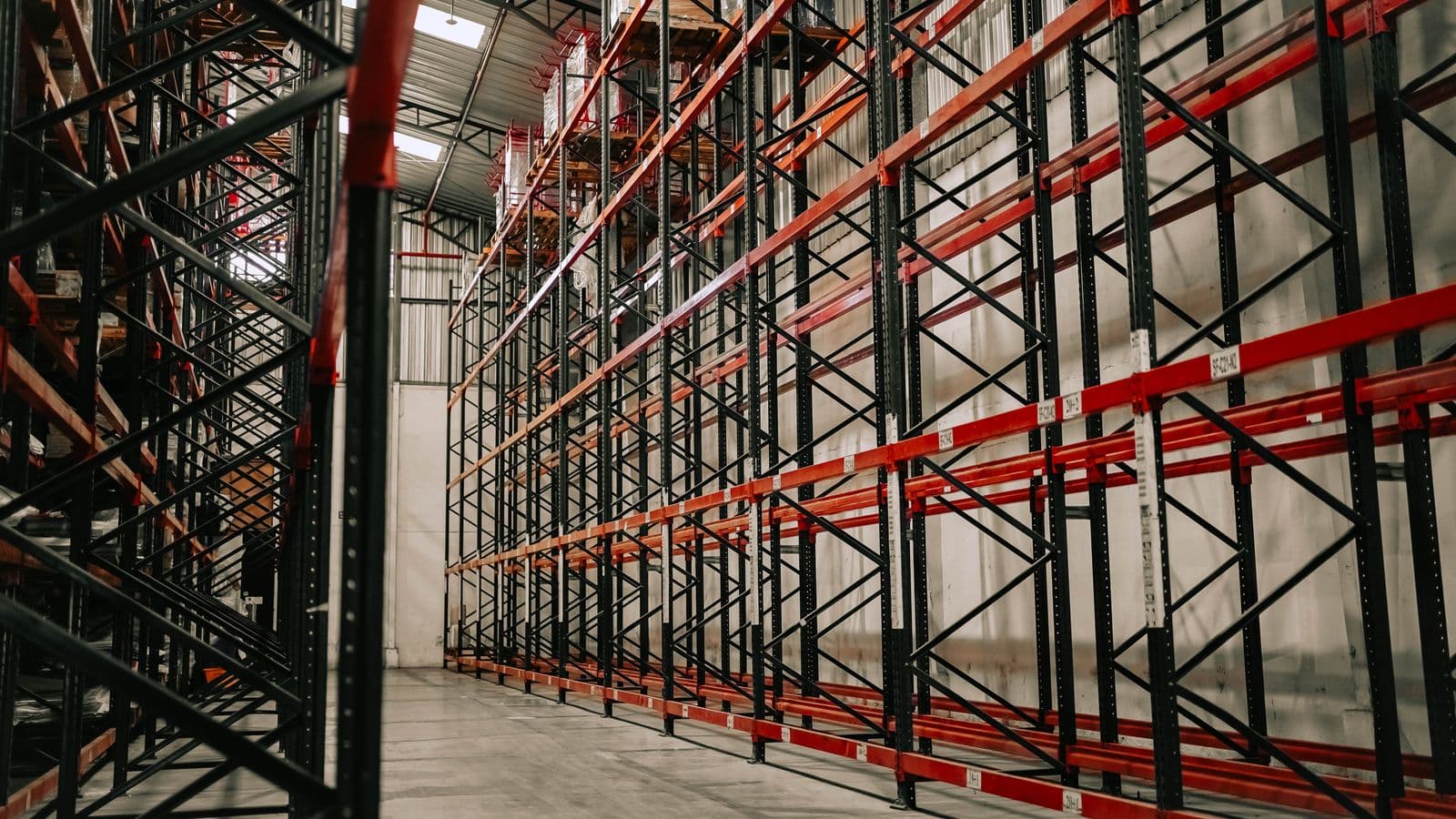 Tall red and black pallet racking lining an empty warehouse aisle