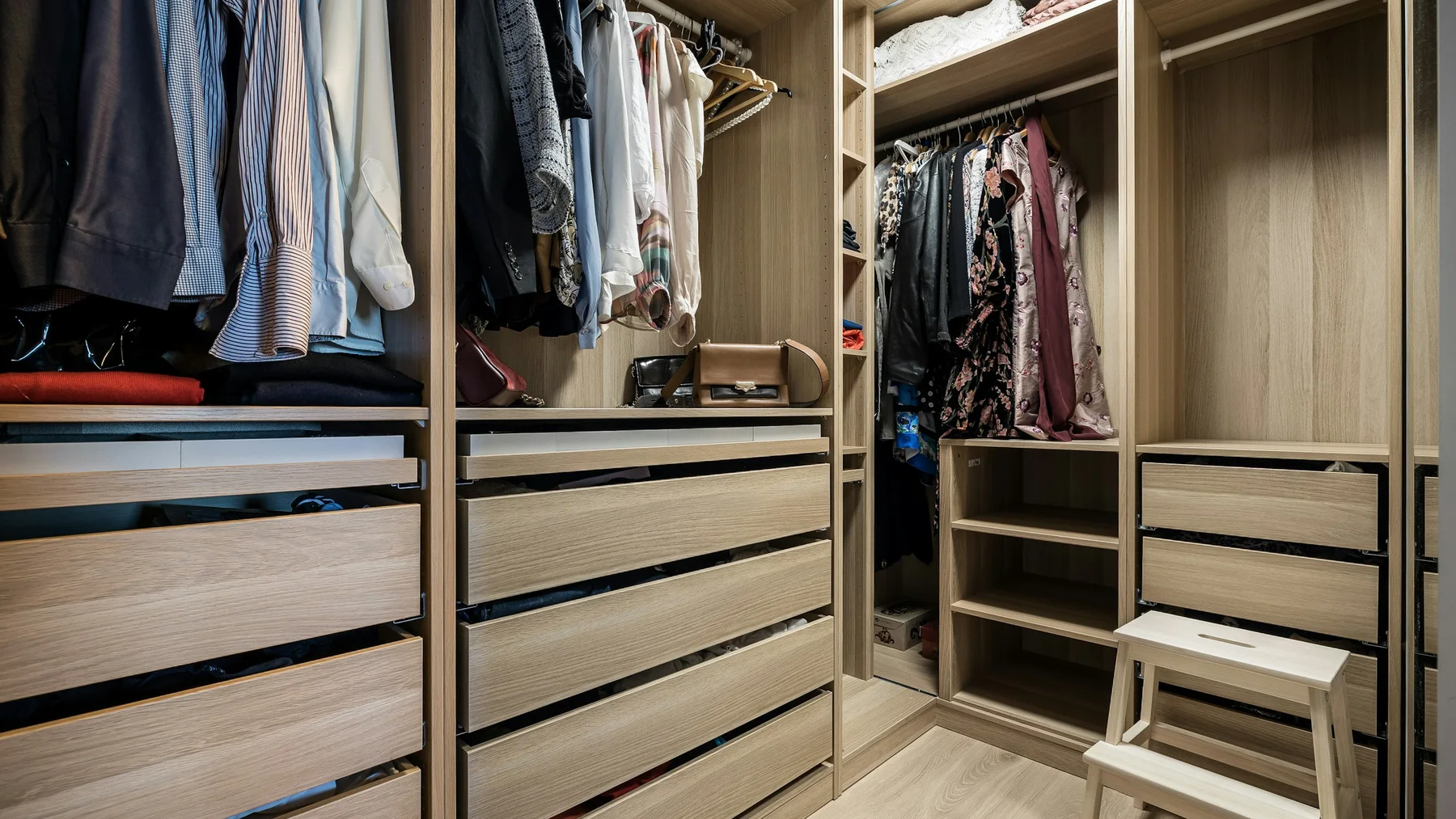 Fitted walk-in wardrobe in an apartment with hanging clothes, open drawers and empty shelving