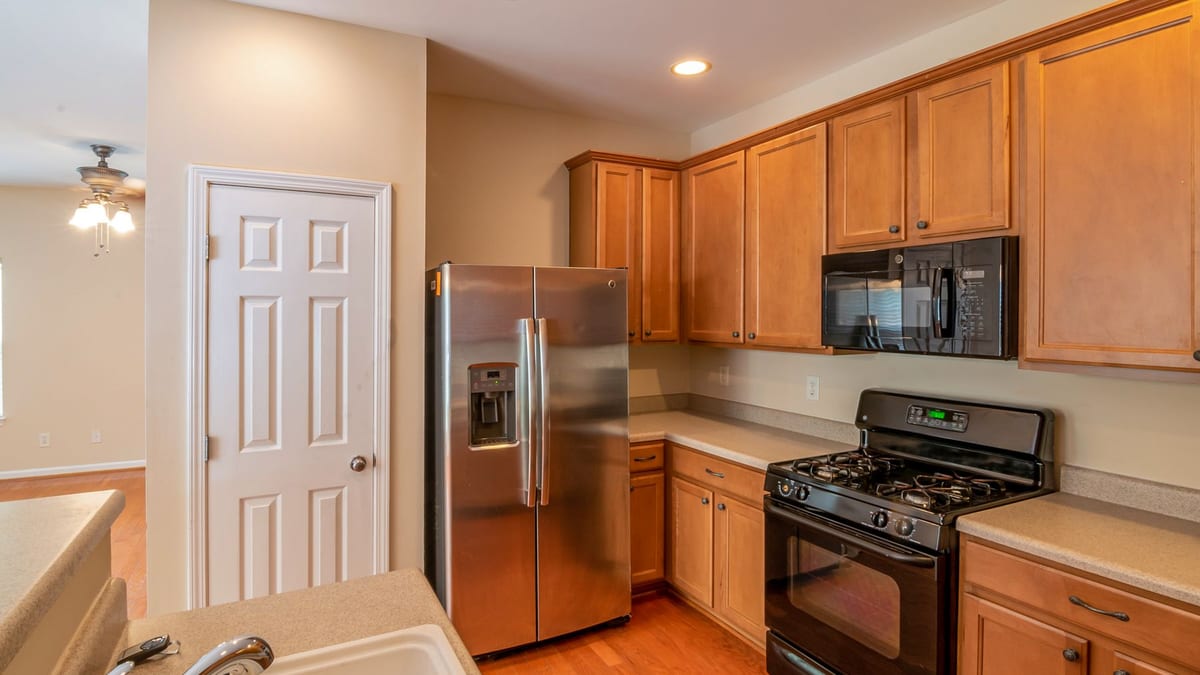 Stainless steel side-by-side refrigerator and a black gas stove built into a fitted kitchen with wooden cabinetry