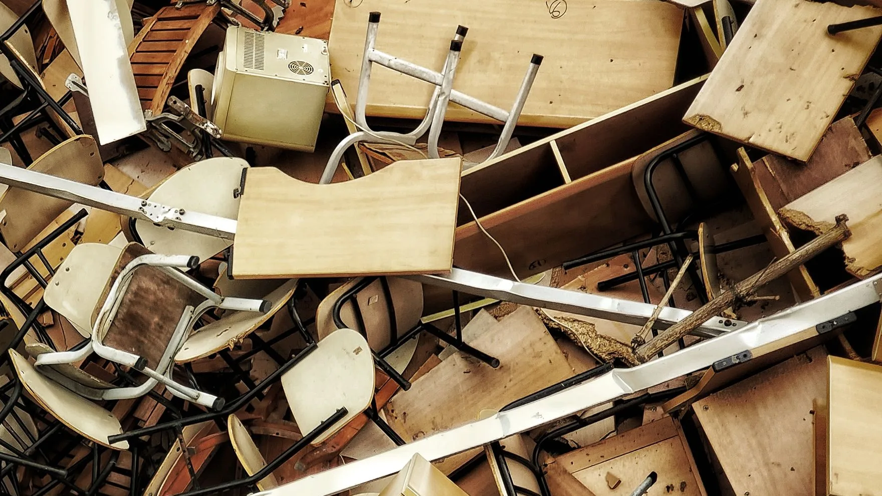 Overhead view of a dense pile of discarded chairs, timber desks and metal frames heaped together