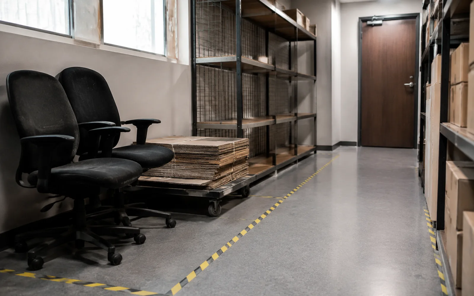 Retired office chairs and flattened cardboard on a trolley beside a clear commercial storeroom aisle