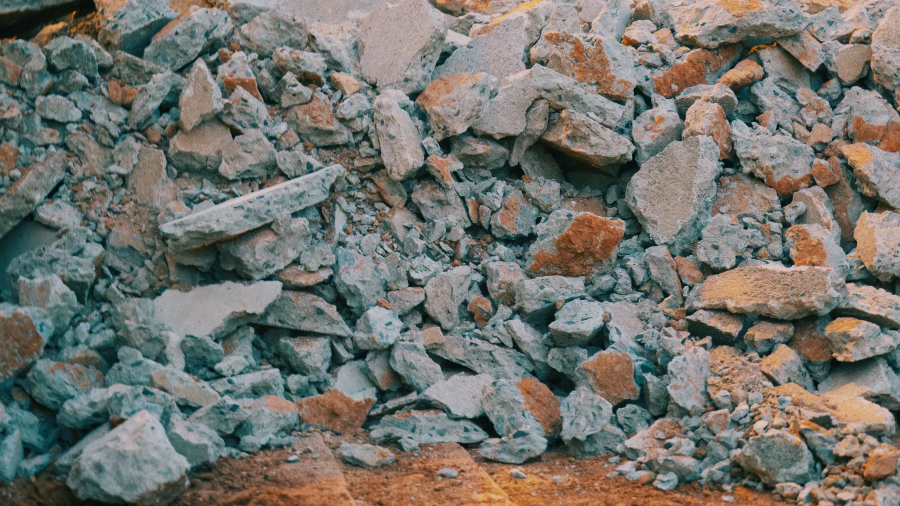 Pile of broken grey concrete and terracotta brick fragments heaped on sandy ground