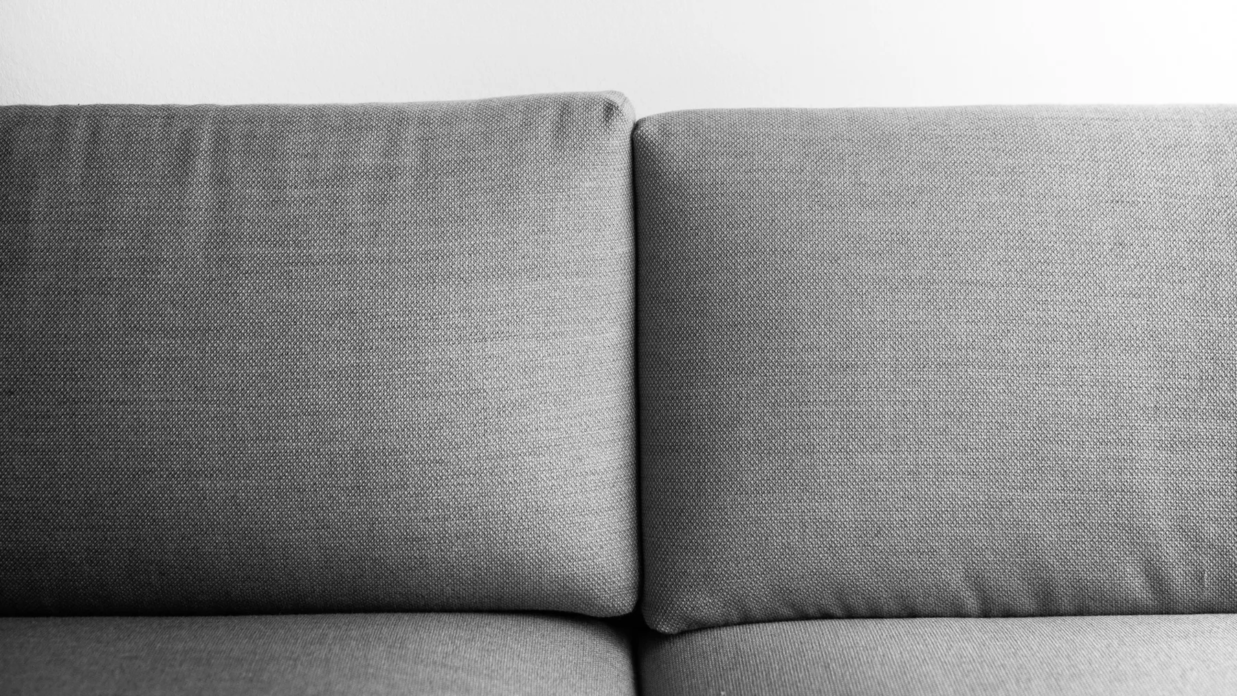 Close-up of two grey upholstered sofa back cushions against a plain white wall
