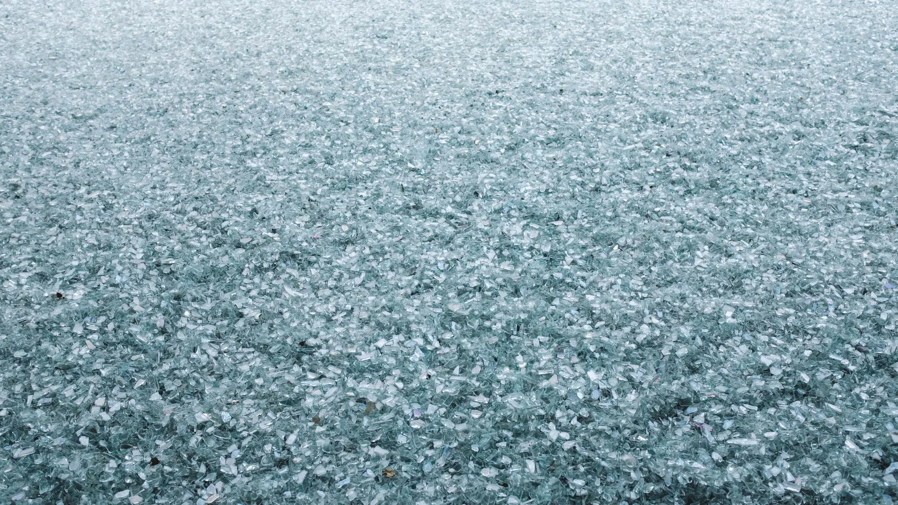 Dense field of crushed pale green glass cullet, thousands of small fragments filling the frame