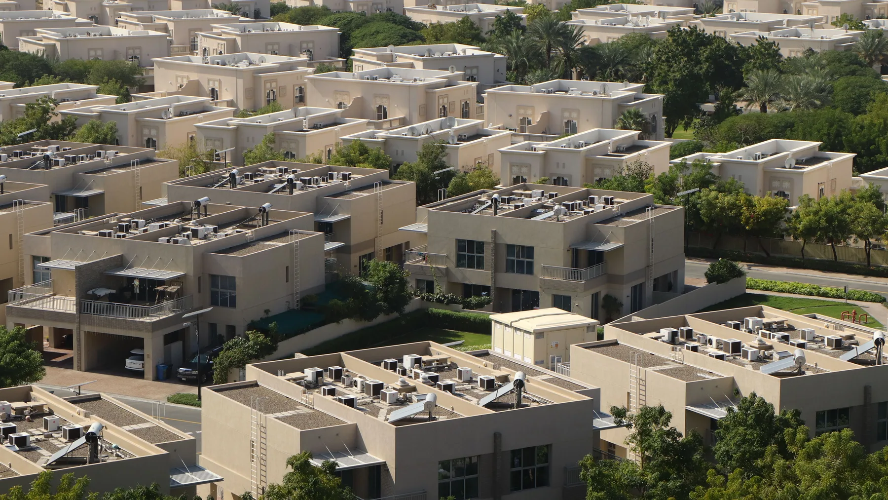 Aerial view of a Dubai villa community with flat sand-coloured rooftops, air conditioning units and landscaped streets