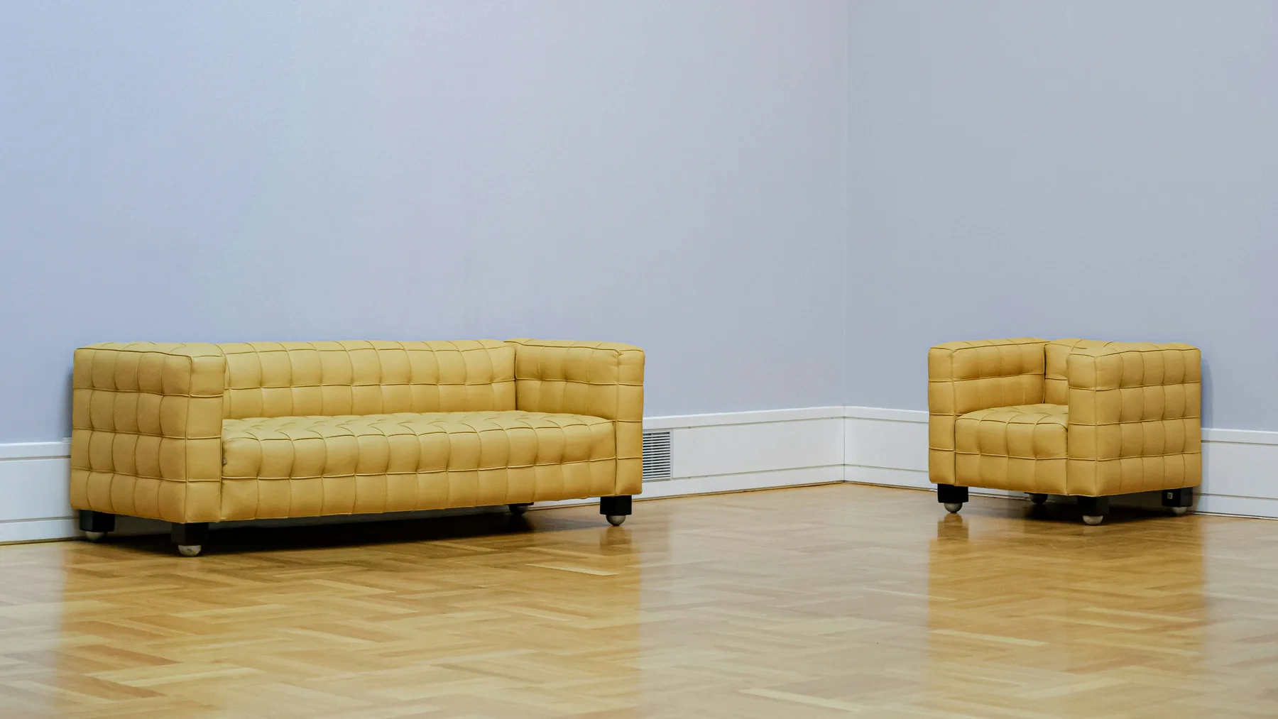 Tan leather sofa and matching armchair left standing alone against the walls of an emptied room