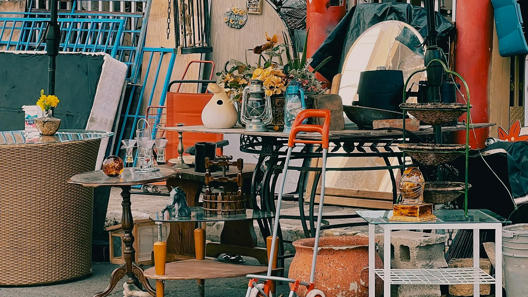 Second-hand side tables, glassware, planters and a mirror set out together on a paved area after a sale