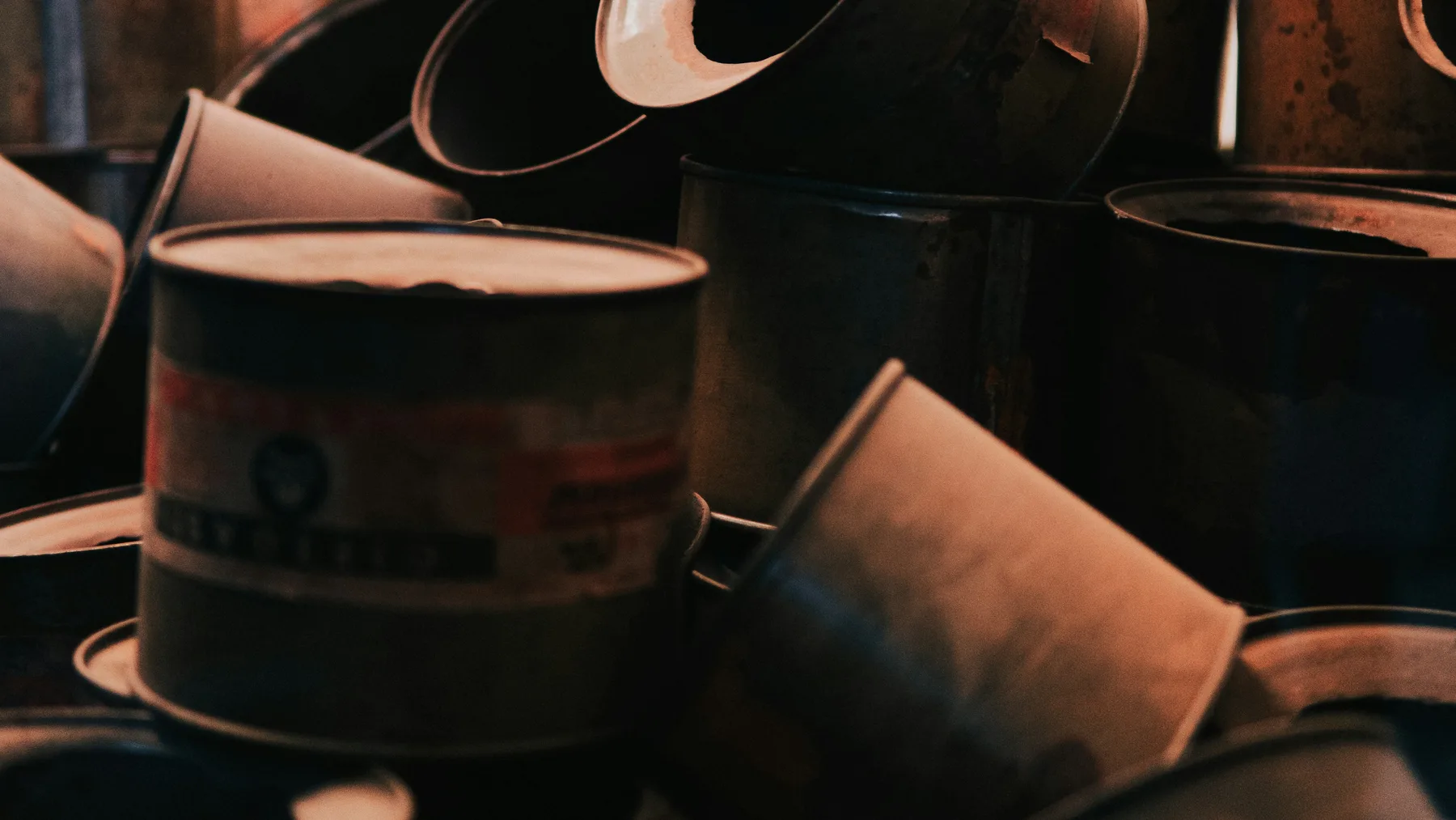 A heap of discarded metal paint and solvent tins with rusted rims and labels worn away