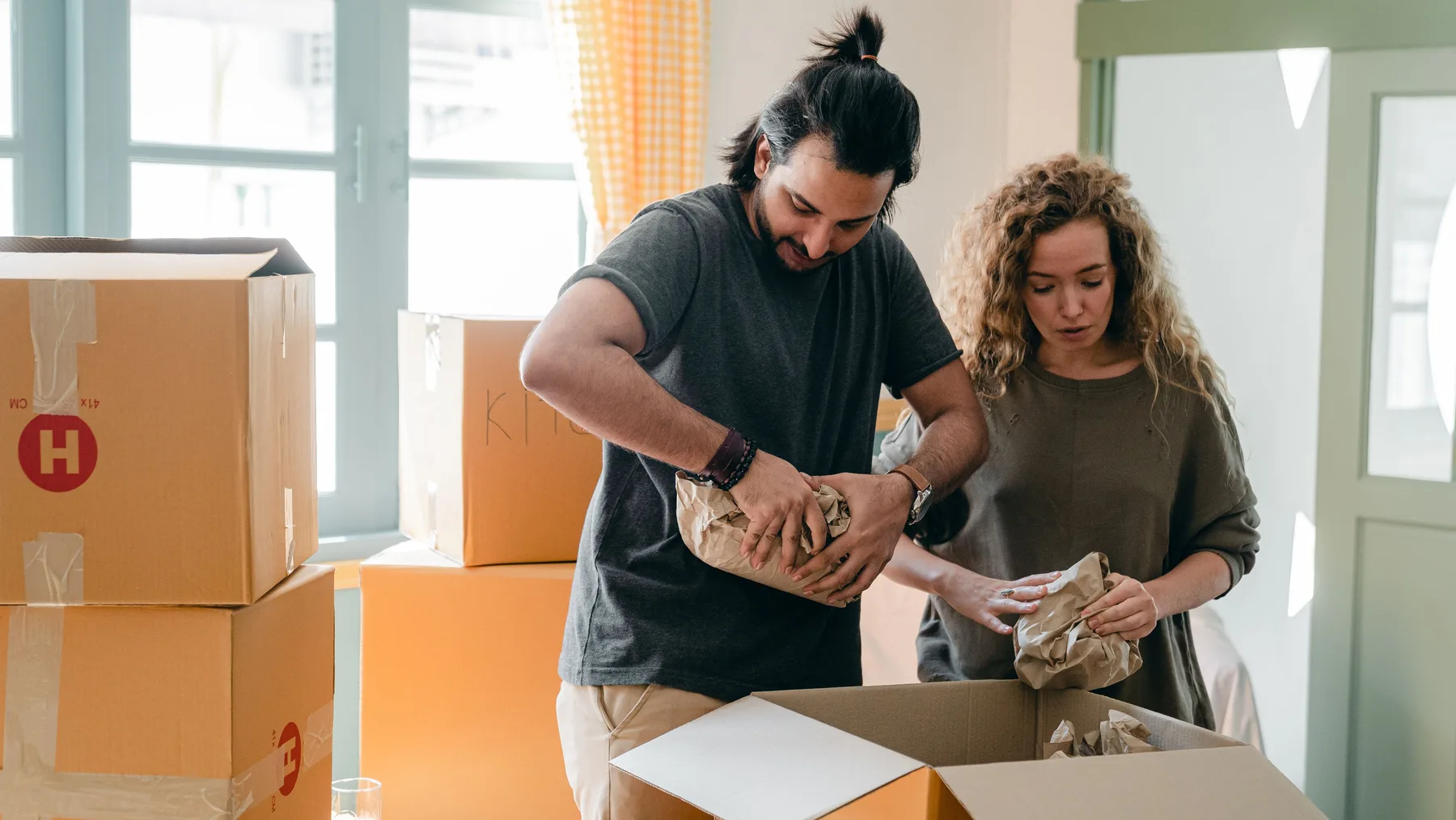 A person carefully unpacking, inspecting, and sorting boxed household items in an organised room