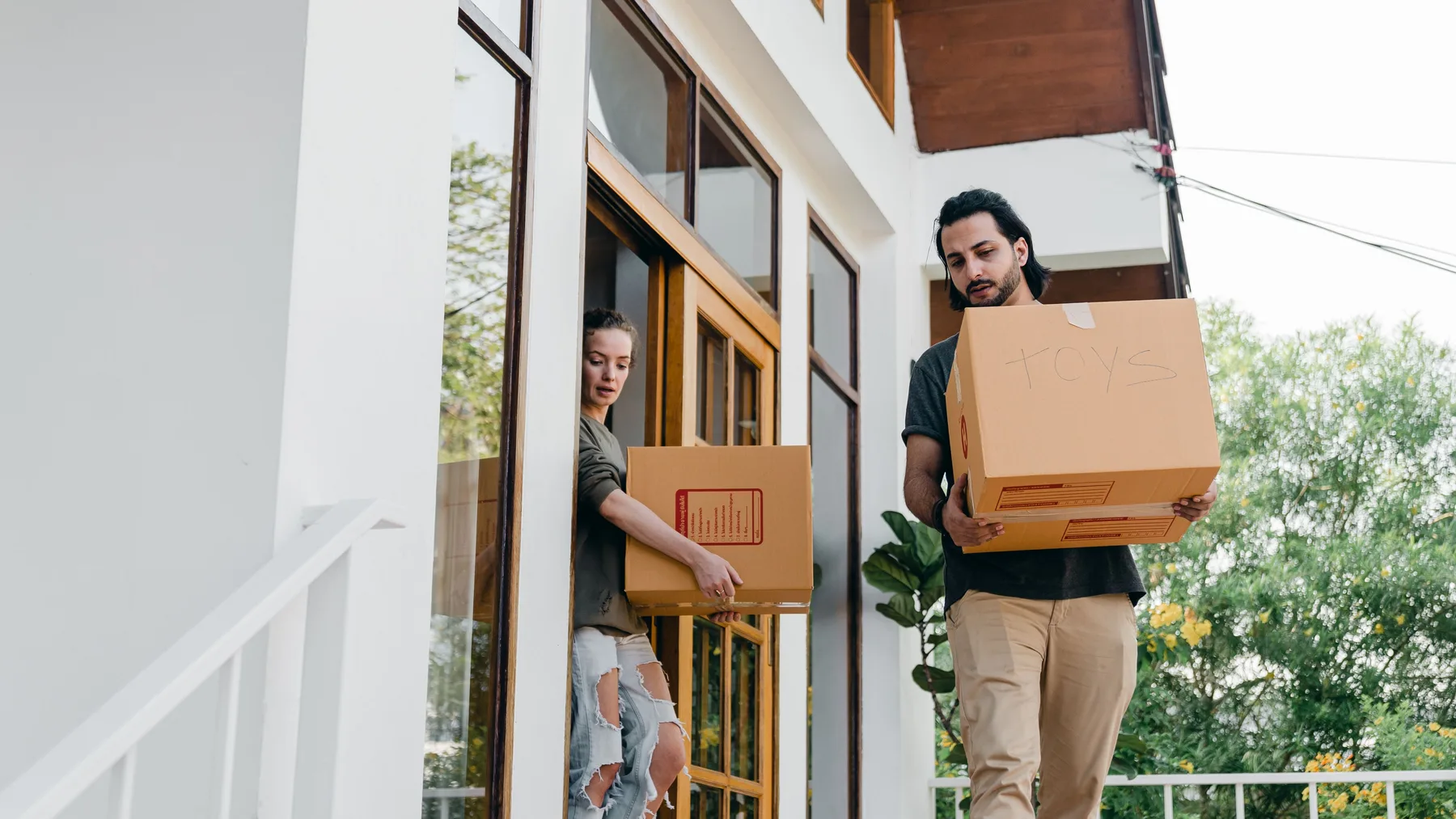 Couple carrying packed cardboard storage boxes out of a house during cleanout