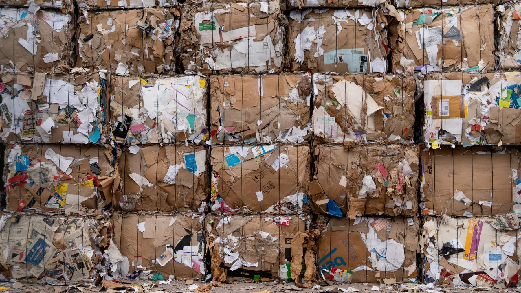 Wall of baled and wire-bound cardboard and paper stacked several bales high at a recycling yard