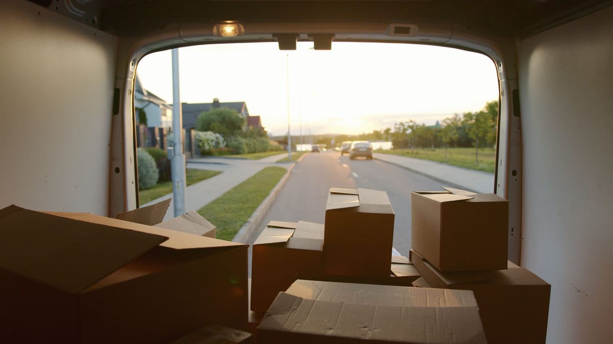 Cardboard boxes loaded inside a van's cargo area, with a residential street visible through the open rear doors