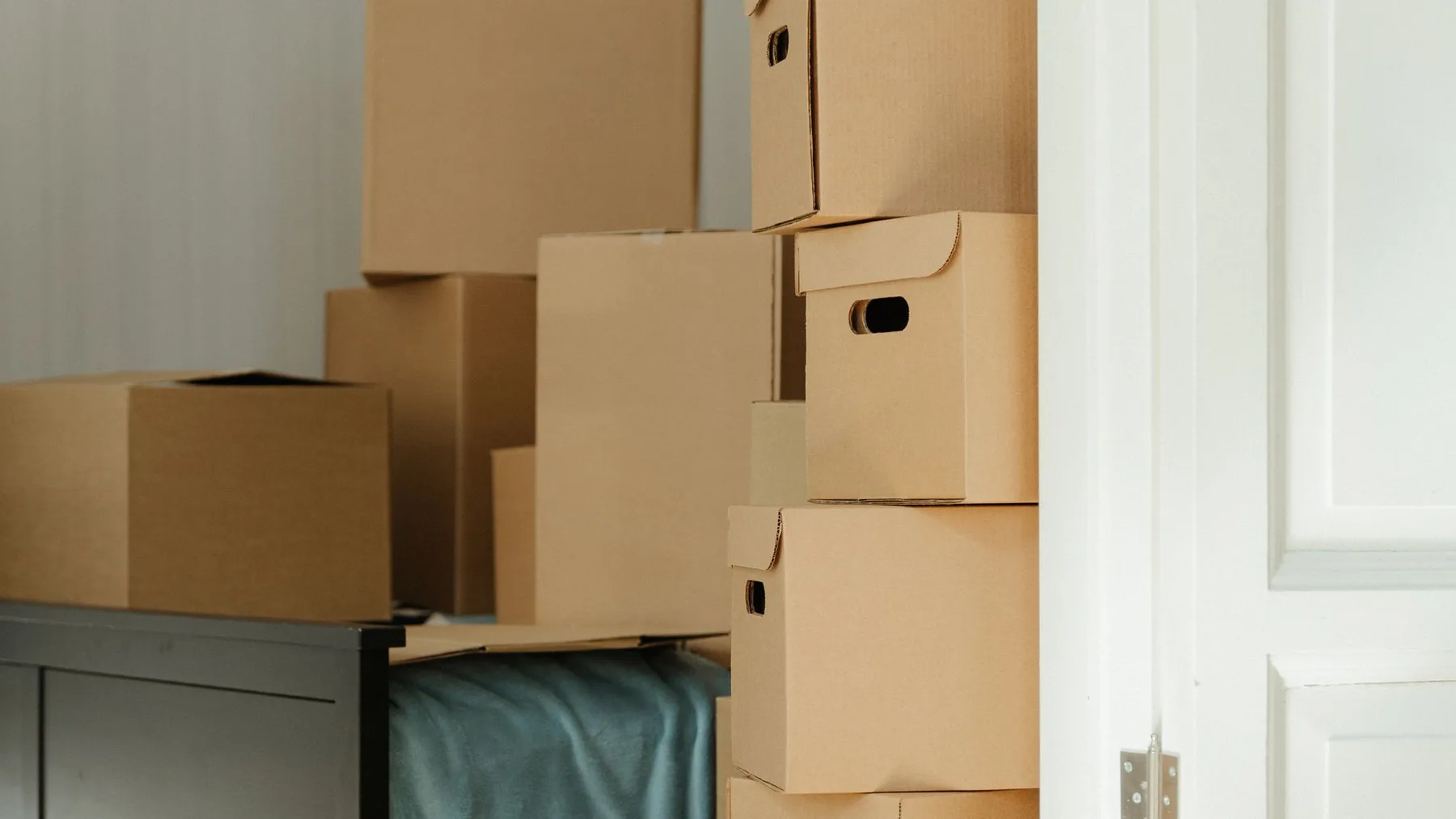 Stacked cardboard storage boxes and a sideboard beside an open door in a home