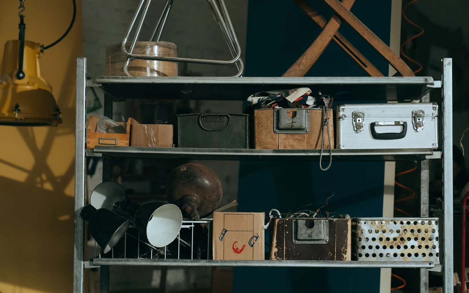 Metal shelving in a store room holding old boxes, cases, lamps and a folded ironing board