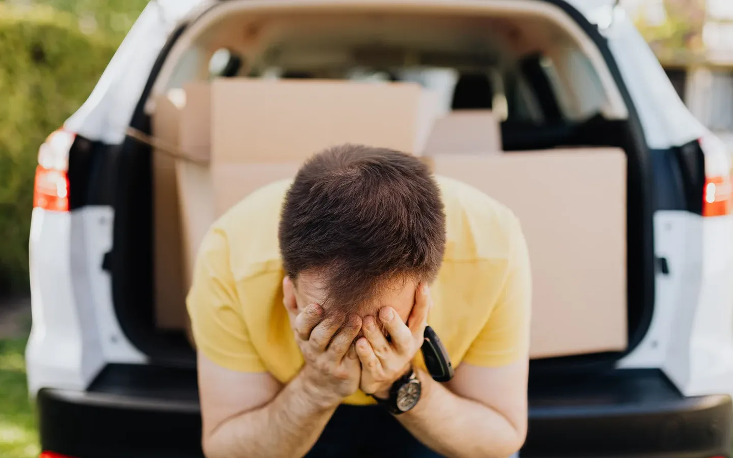 Frustrated man with his head in his hands at the open boot of a car packed full of cardboard boxes