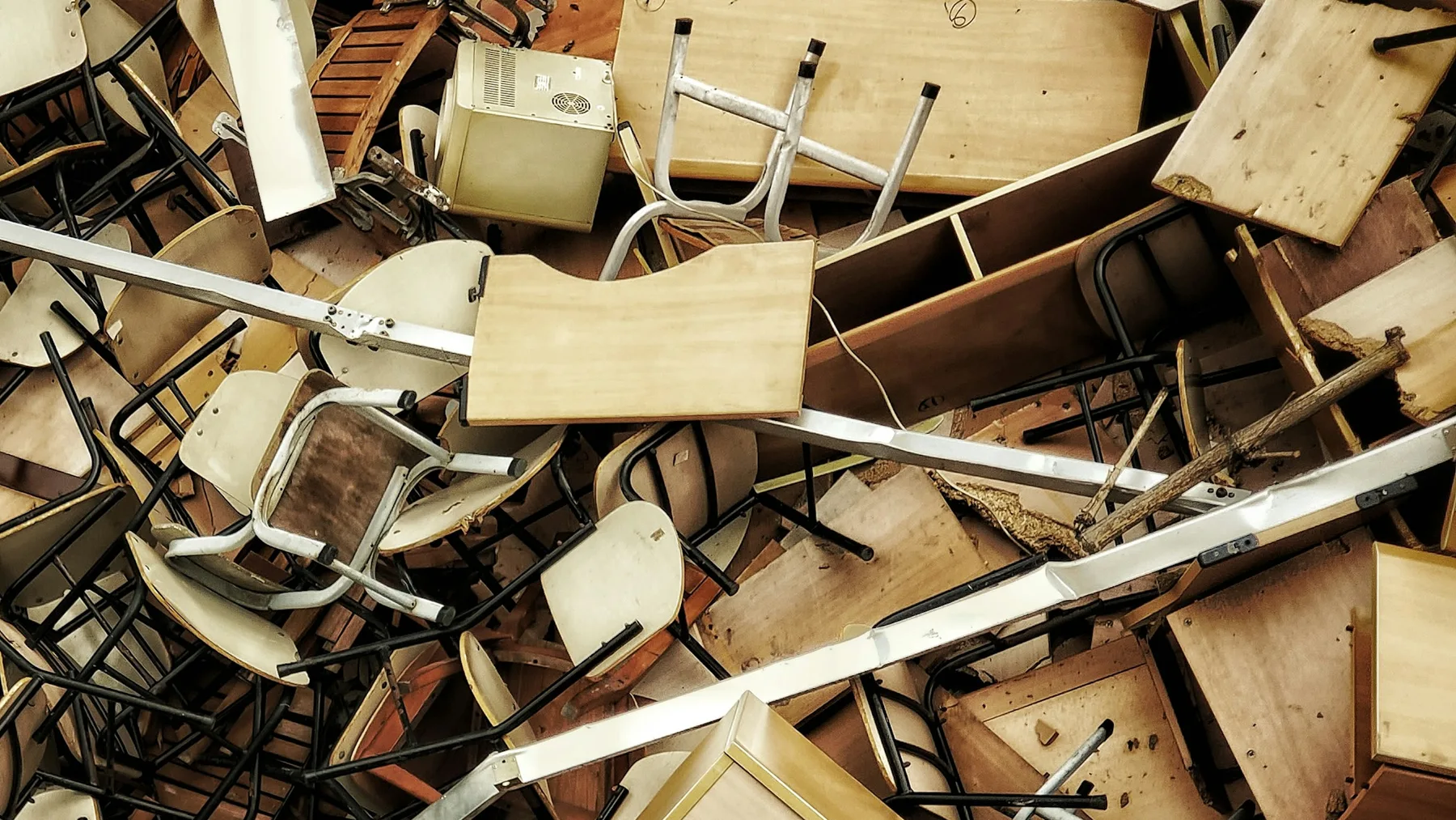 A dense heap of discarded wooden and metal chairs, desks and table tops piled on top of each other