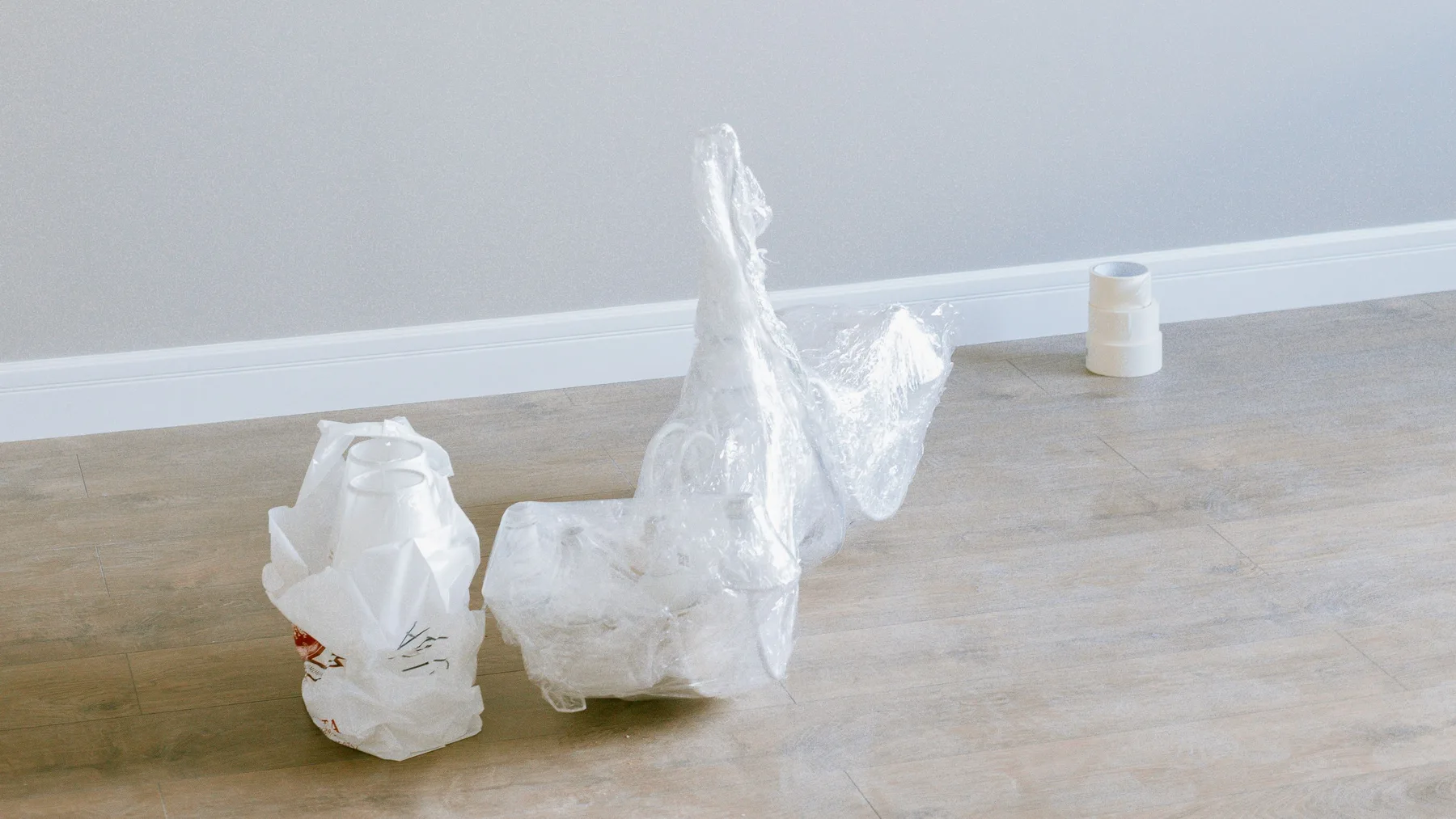 Leftover plastic wrapping, a bag of packaging and a roll of masking tape on the floor of an empty finished room