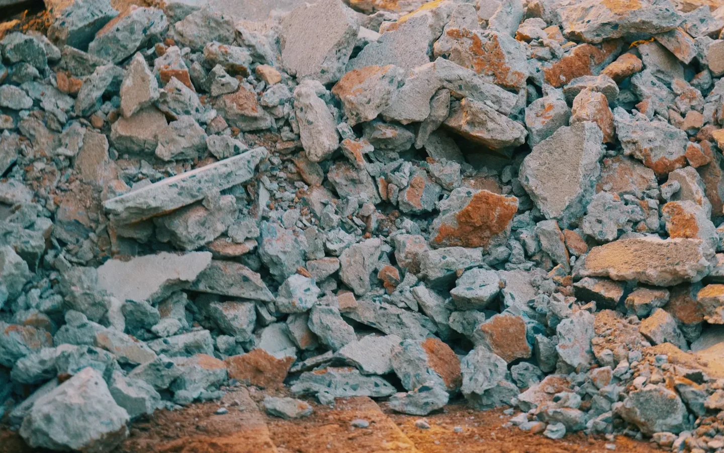 Pile of broken grey concrete and terracotta brick fragments heaped on sandy ground