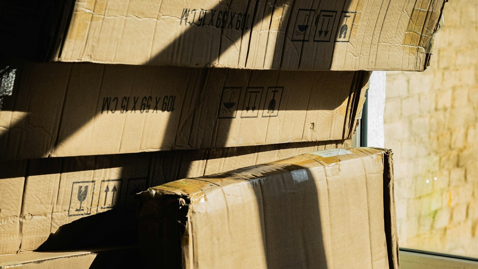 Stack of flattened cardboard boxes with shipping labels leaning against a wall in bright sunlight