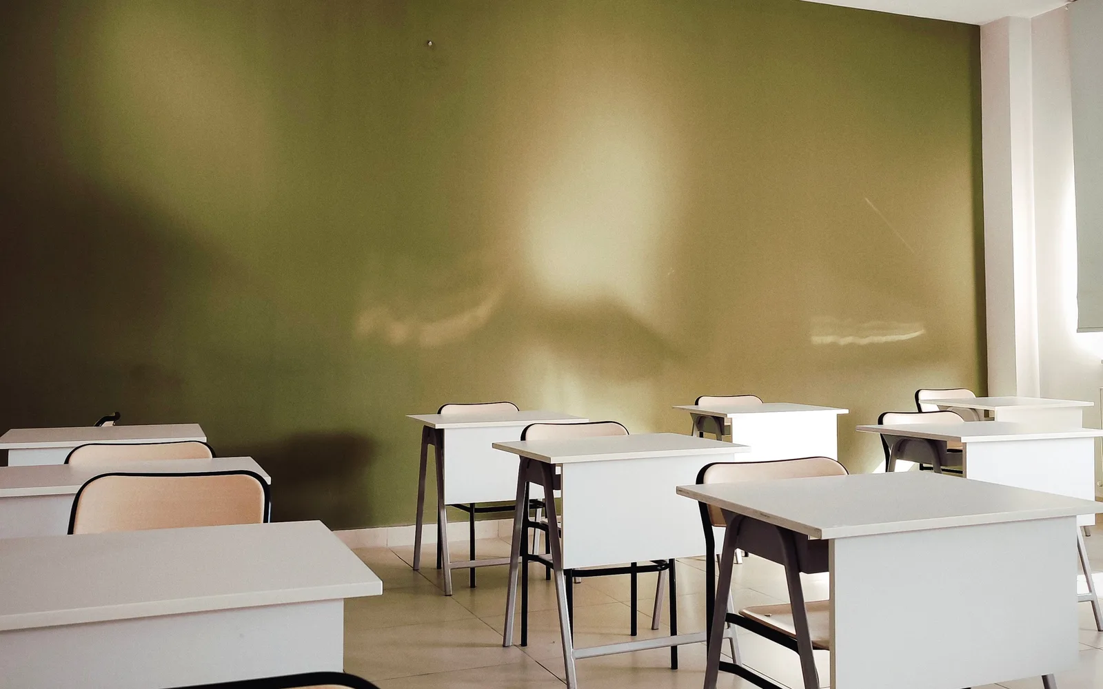 Rows of white student study desks and wooden chairs inside an educational classroom