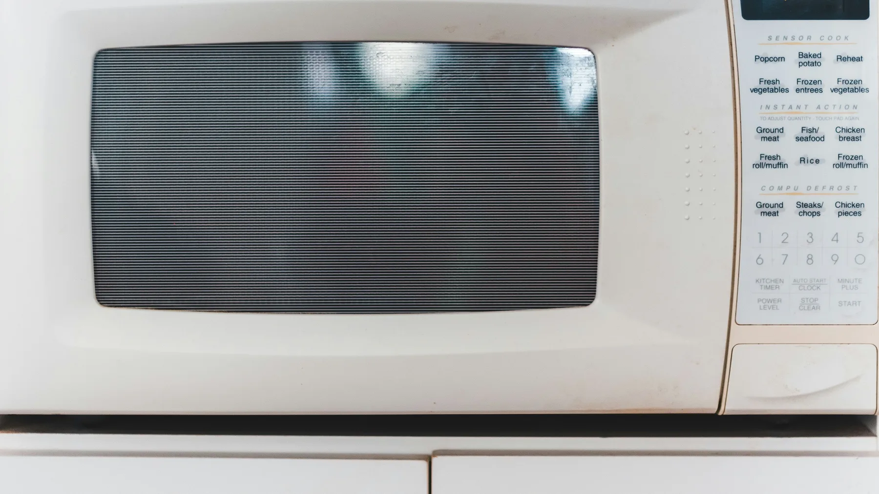 Close-up of a white microwave oven's door and control panel showing worn edges