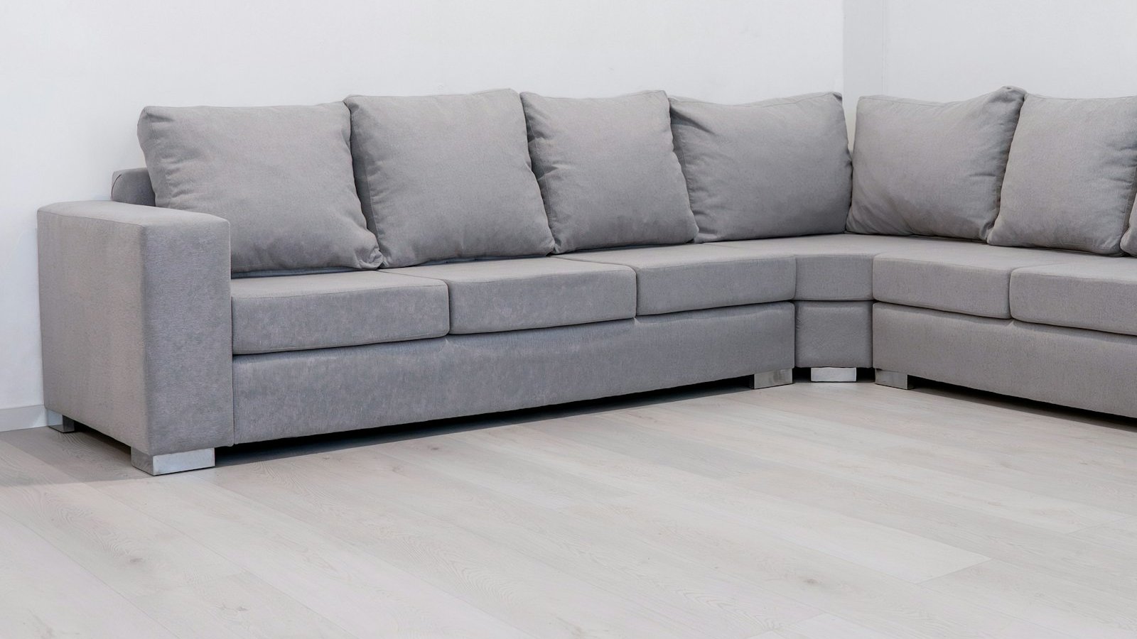 Grey fabric L-shape sectional sofa with matching cushions in an empty room with white walls