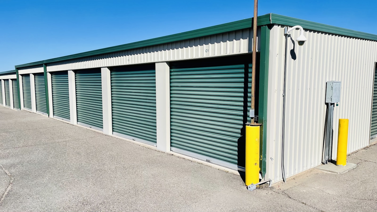 Row of green roller-shutter doors along a single-storey self-storage building under a clear sky