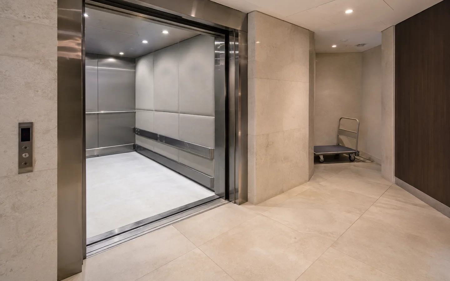 Open padded service lift with a clear tiled approach and a furniture dolly parked in a side recess
