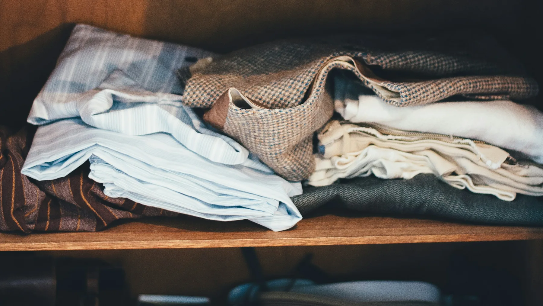 Folded shirts, tweed jackets and knitwear packed tightly together on a wooden cupboard shelf