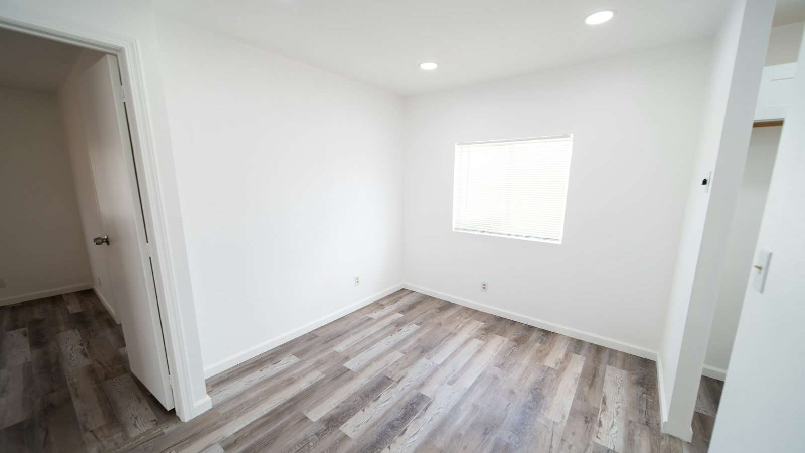 Empty villa bedroom with light wood-look flooring, white walls and a window, cleared of all furniture