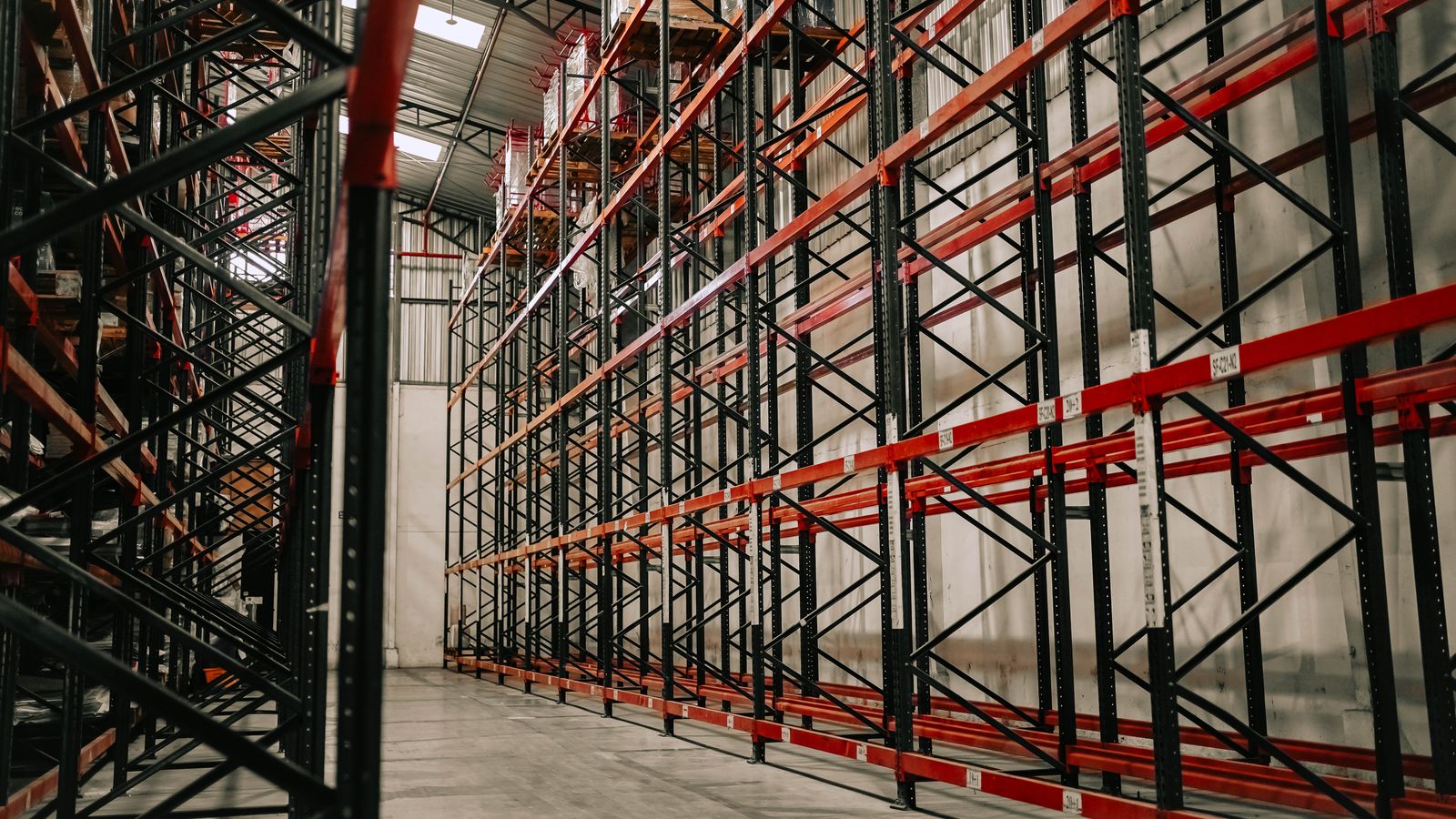 Tall red and black pallet racking lining an empty warehouse aisle